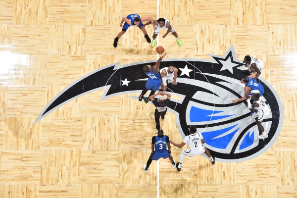 An aerial view of a basketball court with the Orlando Magic logo and players mid-action on top of it. 