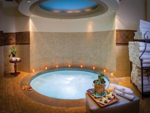 A small indoor jacuzzi with floral accents, candles, and a table set with sparkling wine and chocolate covered strawberries.