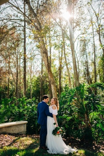 A man in a suit holds a woman in a long, white dress close with a background of tropical plants and trees. Rosen Plaza has plenty of nature-rich photo locations for your Orlando destination wedding.