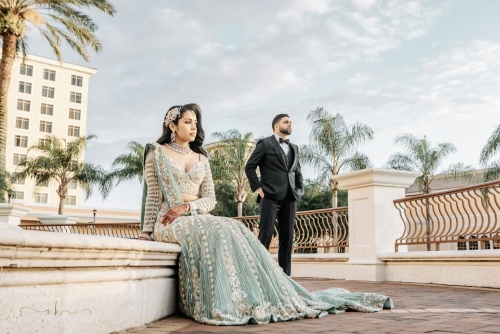 A woman in a light blue sari sits on the side of an outdoor fountain with a groom standing behind her. Rosen Shingle Creek is the perfect elegant venue for an Orlando destination wedding,