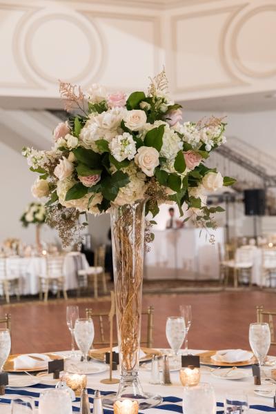 A tall centerpiece with pink roses and hydrangeas set on a round table in front of a dance floor.