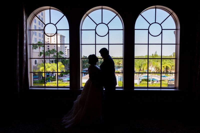 A silhouette of a couple standing face to face on their wedding day in front of windows that show beautiful greenery and views of Rosen Shingle Creek. 