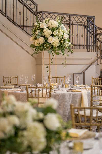 A tall floral arrangement with white hydrangeas on a table in front of a staircase with a wrought iron railing.