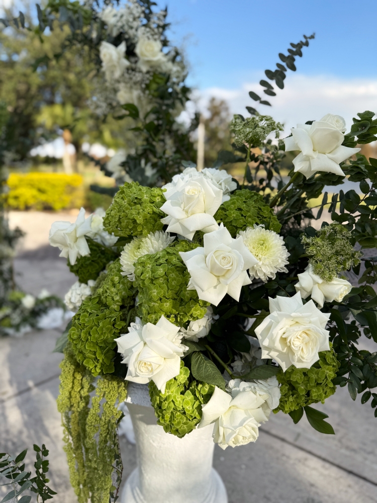 A close-up of an arrangement with green hydrangeas, amaranths, white roses, and other greenery.