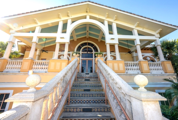 A staircase with tiled stairs and a stone railing leading up to a building with craftsman style pillars. 