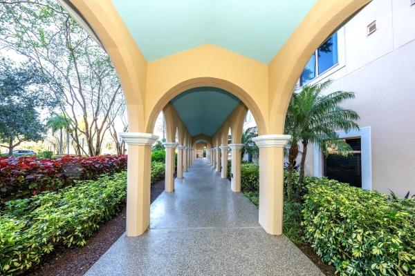 A paved walkway with cream-colored arches and a light blue ceiling between landscaped bushes. The Breezeway is a great option for a first look at Rosen Shingle Creek.