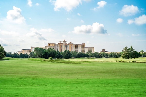 An exterior shot of a large hotel in the distance surrounded by trees and rolling green hills. 