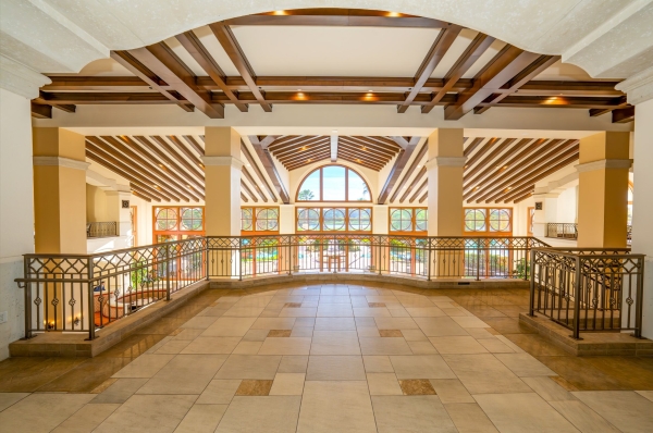 An interior balcony overlooking large dark wooden beams on the ceiling leading to two-story windows overlooking a beautiful courtyard.