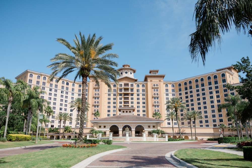 The exterior of Rosen Shingle Creek, a towering hotel with palm trees and a fountain, the perfect destination for a hotel wedding.