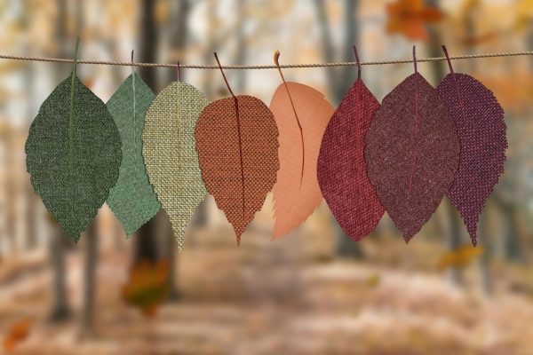 An array of autumnal colored leaves cut out of fabric hang on a piece of twine in a fall forest setting.