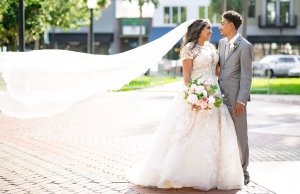 A bride wearing a ballgown wedding dress holding the groom wearing a gray tuxedo.