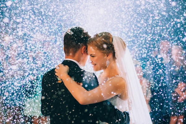 A bride and groom embrace surrounded by a flurry of white confetti. 