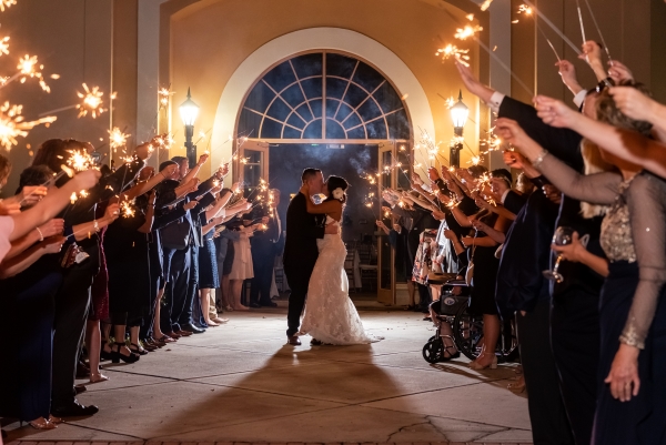 A bride and groom sharing a kiss surrounded by wedding guests waving sparklers.