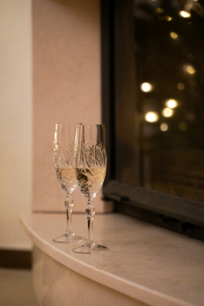 Two engraved Champagne flutes with sparkling wine in them sit on a marble windowsill beside a dark window.  