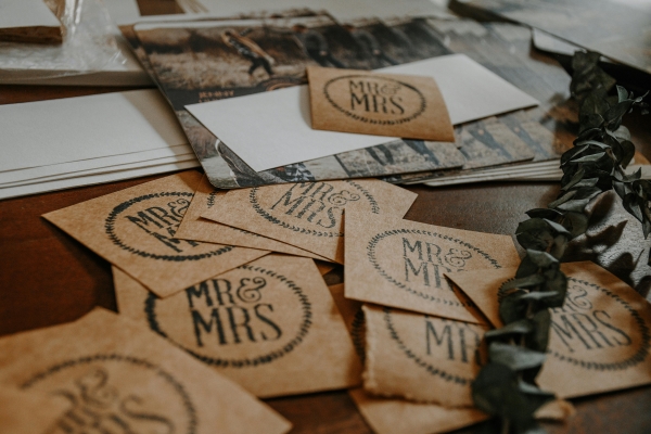 A close-up of brown rustic cards with Mr. & Mrs. stamped on them resting on a table with a sprig of eucalyptus.