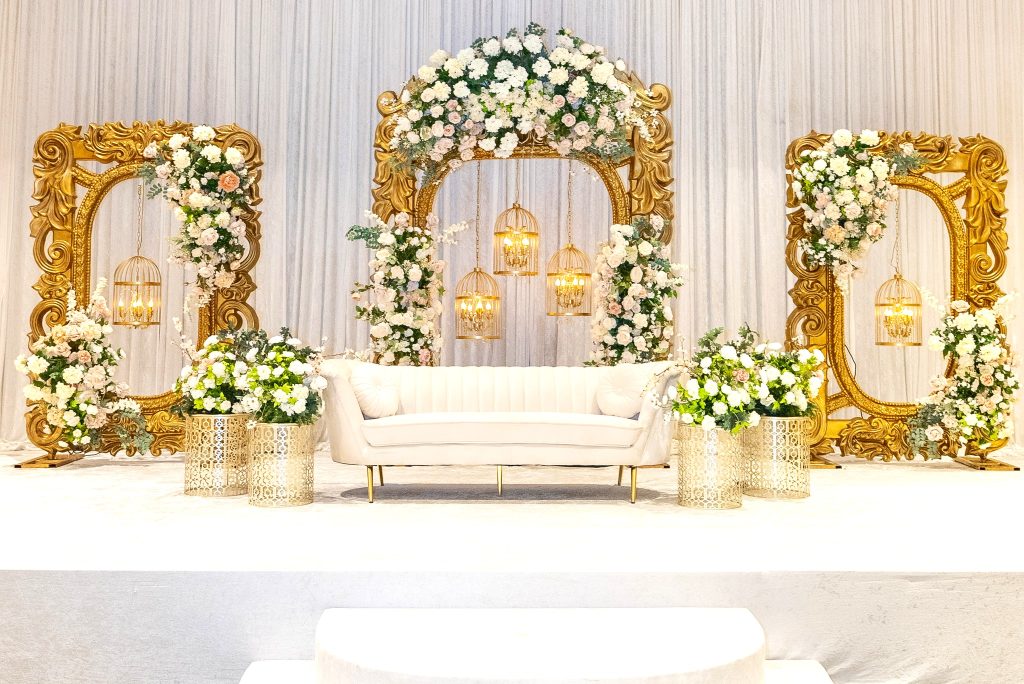 Three golden arches on a stage with a backdrop of white drapery, decked out in white roses and gold bird cages. 