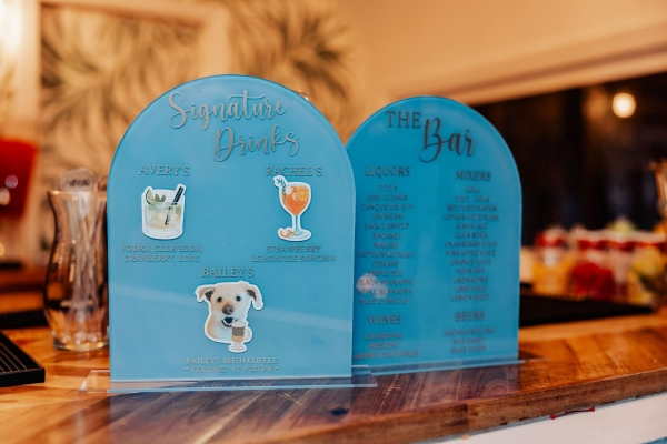 Two blue arched acrylic signs with stickers, including the face of a dog, and a drink menu. Name a drink after your furbaby to include your pet in your wedding day. 