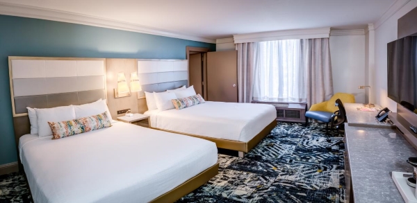 Two queen beds with white linens and modern headboards in a hotel room with a contemporary dark patterned carpet.