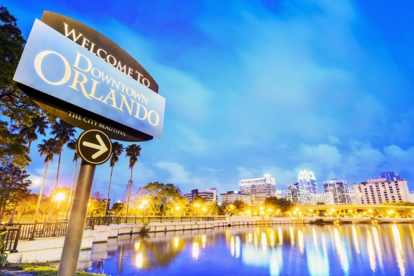 A glowing lake reflecting the lights of the building and surrounding streets beside a sign that reads Welcome to Downtown Orlando with an arrow.