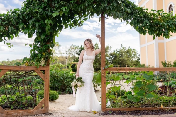 A bride poses beneath an archway of greenery at Emma's Creekside Farm, a garden at Rosen Shingle Creek.
