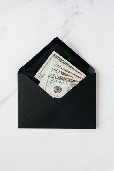 A black envelope with several folded twenty-dollar bills against a white marble background.  