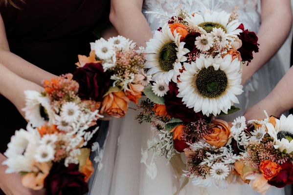 A closeup of autumnal bouquets held by a woman in a white dress and three other women in red dresses.
