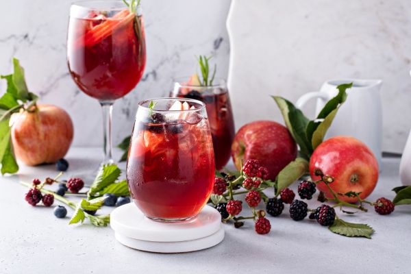A red sangria cocktail in different shaped wine glasses surrounded by apples and blackberry twigs.
