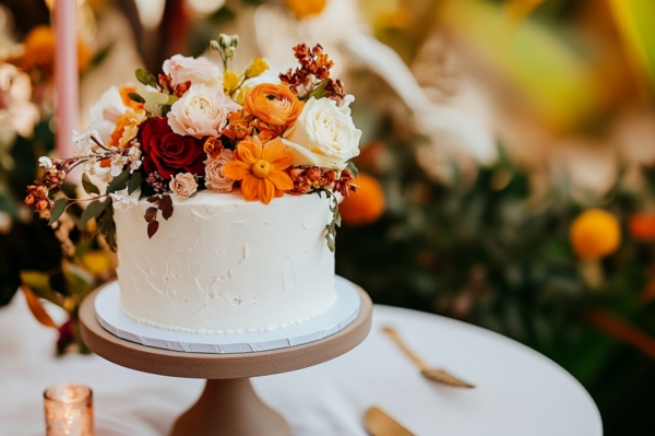 A single-tier wedding cake with white frosting, decorated with autumnal flowers for a fall wedding look.