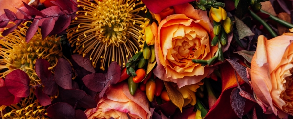 A close-up of a fall bridal bouquet with peach, orange, purple, and dark red florals.