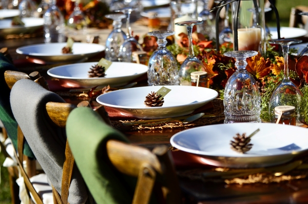 A close-up of table a long table with settings using green linens and pinecones as fall wedding decor.
