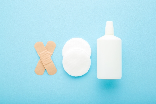 Criss-crossed bandages, white gauze pads, and a white spray bottle against a light blue background.
