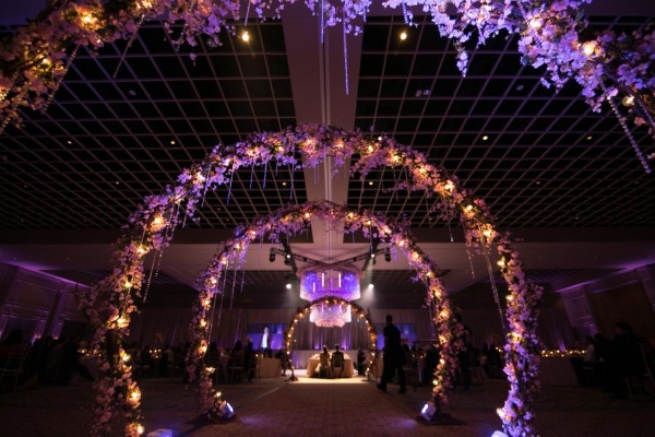 A dark room with moody purple lighting and four glowing archways leading to a dramatic chandelier. 