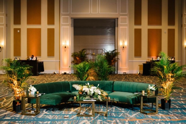 Green velvet sofas surrounded by houseplants and dramatic floral displays in a large, spacious ballroom.