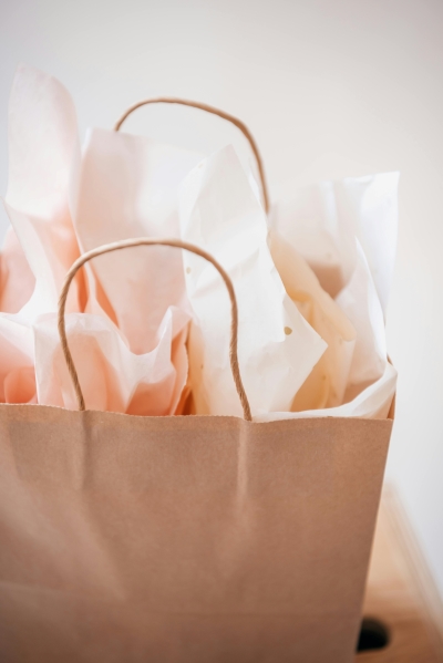 A light brown paper gift bag stuffed with light pink tissue paper.  