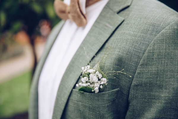 A close-up of a man's sage green suit pocket with baby's breath.