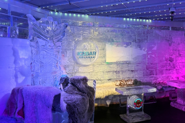 A room made of ice with blue and purple lighting, a large ice sculpture, and a table made of ice at ICEBAR Orlando.