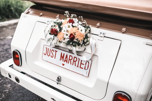 The back of a vintage car with a license plate that reads Just Married and a flower arrangement above it.