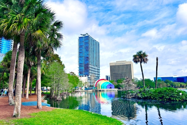 Lake Eola in Orlando, with the rainbow painted amphitheater, palm trees, and tall corporate buildings on the skyline.