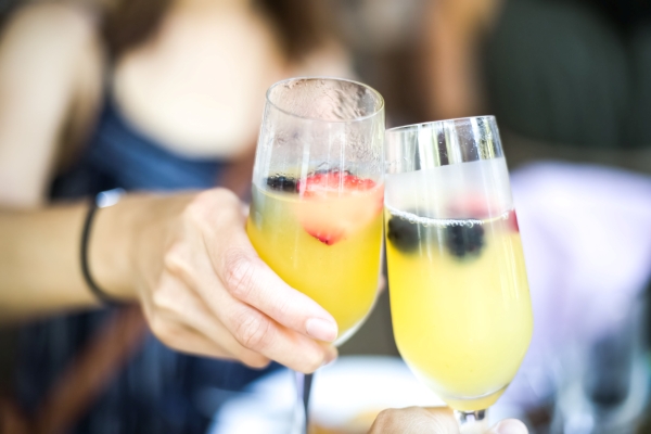 A close-up of two hands toasting mimosas in champagne flutes.