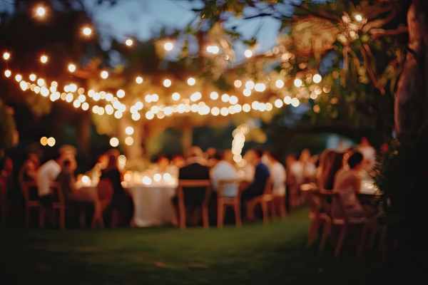 An out-of-focus shot of an outdoor wedding reception table beneath strings of bistro lights.