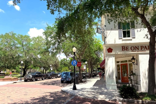 A white storefront surrounded by mature trees along a cobblestone street: Park Ave in Winter Park.