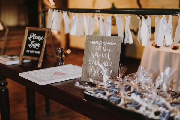 A table with party favors and a sign that reads "Love is Sweet, Please Take a Treat"