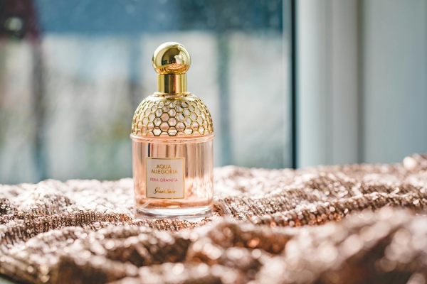 A pink perfume bottle with a golden honeycomb-like top sits on a rose gold sequined fabric.  