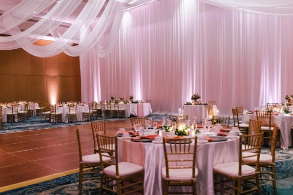 A ballroom with walls of drapery, a dance floor, and round tables decorated with glowing candles.