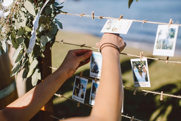 A close-up of hands hanging polaroid photos on a display with twine and mini clothespins.