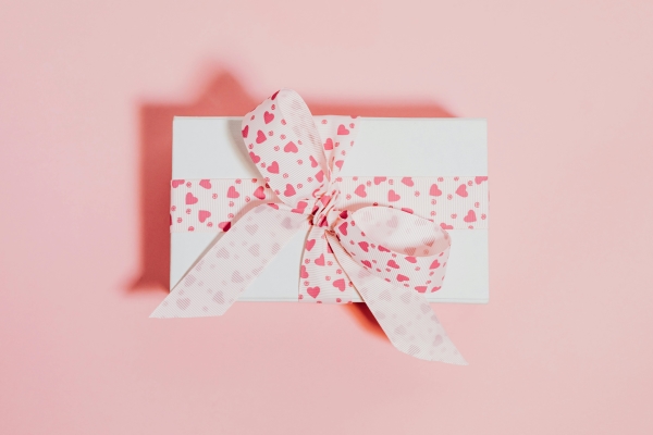 A white gift box wrapped with ribbon with pink hearts against a light pink background.