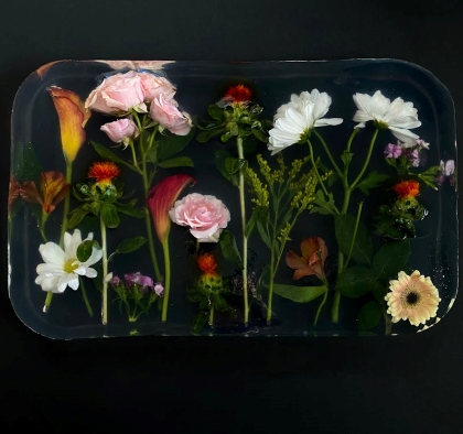 An arrangement of preserved flowers in clear epoxy resin against a dark black backdrop.  