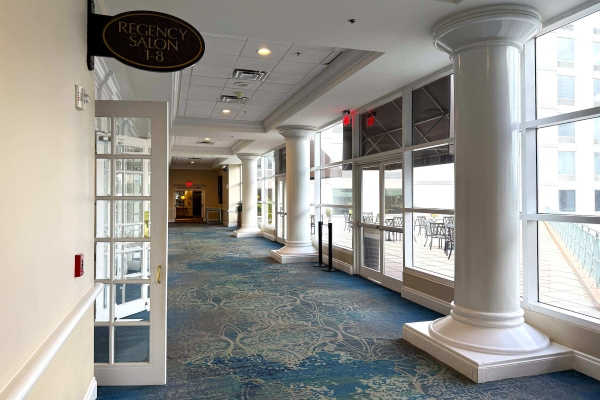 A hallway with French doors, large white columns, and windows and an entrance to an outdoor terrace at Rosen Plaza.
