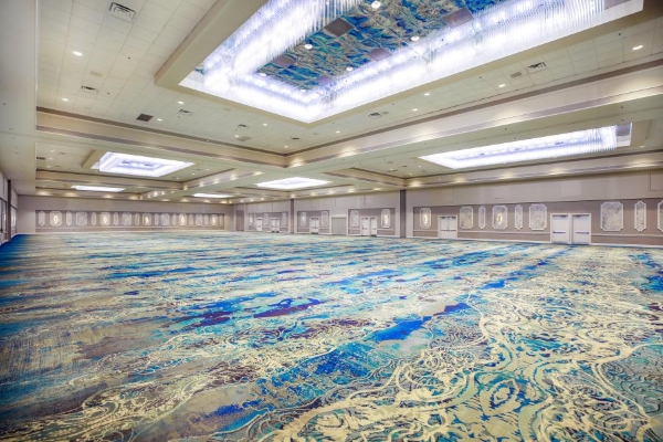 A large ballroom space with blue patterned carpeting and a rectangular chandelier light fixture at Rosen Plaza. The ballroom is a great wedding photo spot.