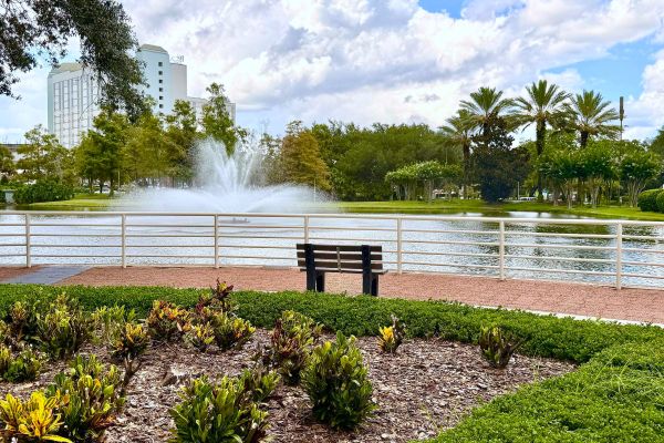 Landscaped gardens and a bench overlooking a large pound with a fountain, barricaded with a white railing.